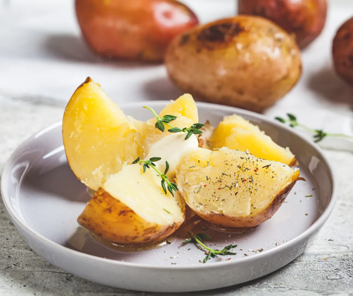 Opengesneden gekookte aardappel op een bord met kruiden